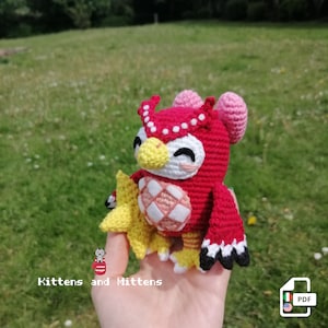 Peut inclure: Peluche hibou en crochet avec un corps rouge, des accents blancs et roses et une étoile jaune. Le hibou tient l'étoile dans son aile droite. Le jouet est assis dans la main d'une personne.