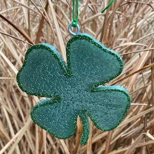 May include: A green four-leaf clover ornament with glitter, hanging from a green string.