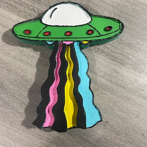 May include: A green and white UFO with red circles on the side, with a rainbow-colored tail trailing behind it.