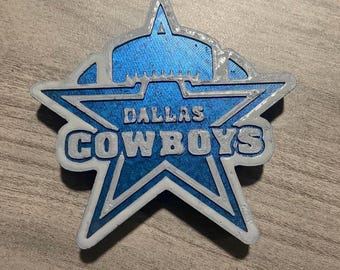 May include: A blue and white 3D printed Dallas Cowboys star logo. The star has a white outline and the words "Dallas Cowboys" are printed in white on the star.
