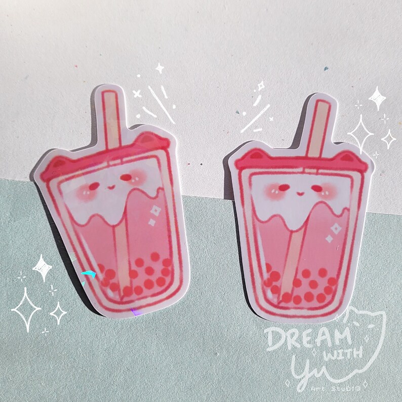 May include: Two pink and white bubble tea stickers with a cute cartoon face and a straw. The stickers have a holographic finish and are surrounded by white stars. The text "DREAM WITH yu" is at the bottom of the image.