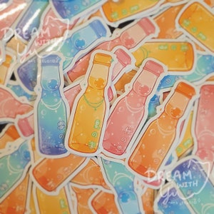 Puede incluir: Una colección de pegatinas coloridas con ilustraciones de botellas de soda ramune japonesas. Las botellas están decoradas con diferentes diseños y tienen texto japonés. El texto en las pegatinas dice "雪の恋", "夏の楽" y "桜の恋".