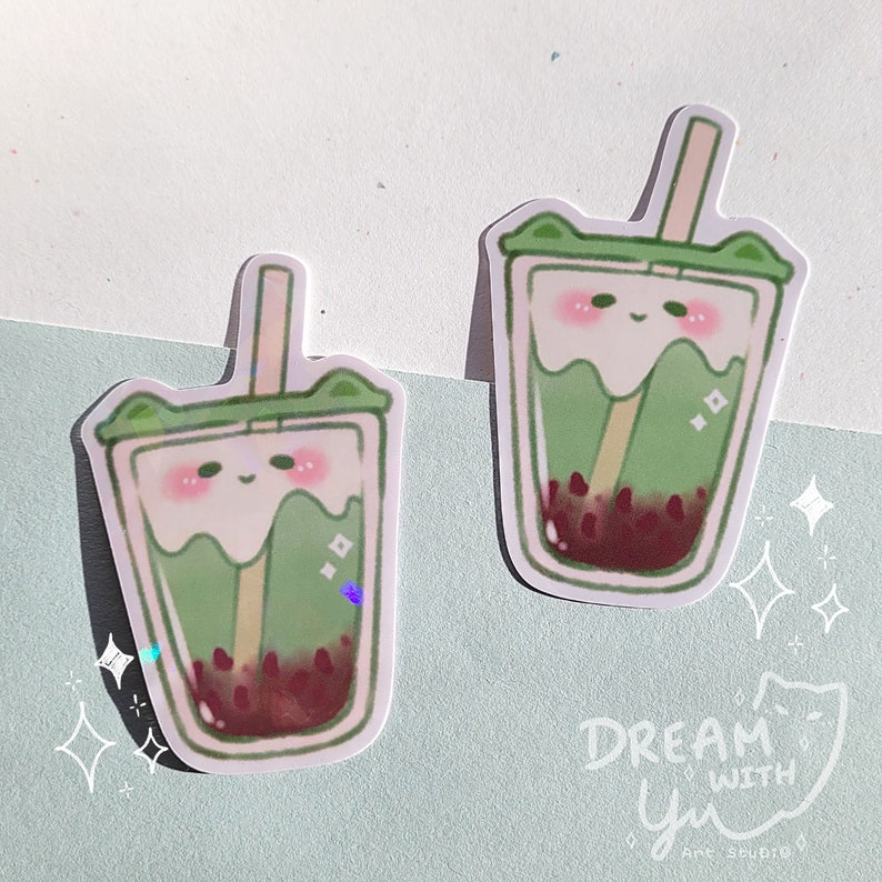May include: Two green and white cartoon bubble tea stickers with a cute face and brown boba pearls. The stickers are on a light blue background with white stars.