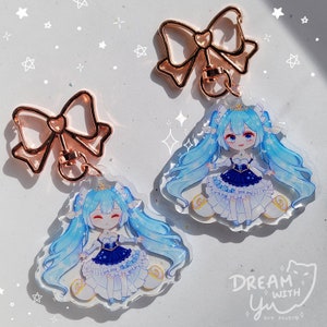 May include: Two blue and white anime character charm keyrings with gold bow accents. The charms feature a girl with blue hair and a blue and white dress. The text "DREAM WITH Yu" is visible in the bottom right corner.