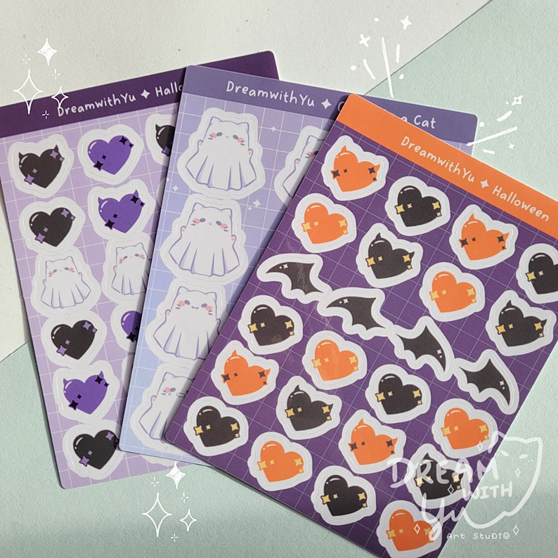 May include: Three sheets of Halloween themed stickers. The first sheet has purple and black hearts with a ghost in the center. The second sheet has a ghost with a white background. The third sheet has orange hearts with bats and the text "DreamwithYu Halloween Cat".