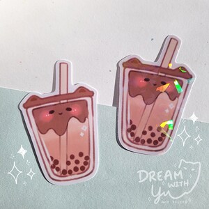 May include: Two holographic stickers of a brown and pink boba tea with a cute cartoon face and black boba pearls. The stickers have a holographic finish and are perfect for adding a touch of whimsy to your laptop, water bottle, or planner.