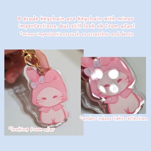 May include: A pink and white character keychain with bunny ears and a bow. The keychain is made of clear acrylic and has a gold chain. The image shows the keychain from two angles, one with the light reflecting off the acrylic and one without.