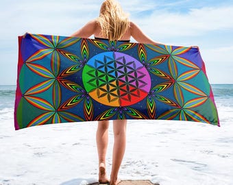 May include: A rectangular beach towel featuring a vibrant, multi-colored geometric pattern. The design centers on a circular flower of life motif surrounded by repeating petal shapes in shades of blue, green, yellow, orange, red, and purple.