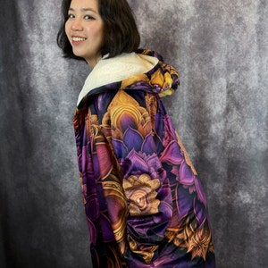May include: A purple and gold hooded fleece blanket with a floral pattern. The blanket is made of soft, plush fabric and features a large hood.
