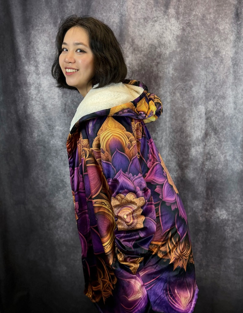 May include: A purple and gold hooded fleece blanket with a floral pattern. The blanket is made of soft, plush fabric and features a large hood.