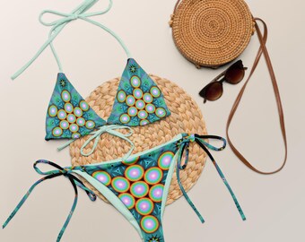 May include: A two-piece bikini set featuring a vibrant teal background with a repeating pattern of concentric circles in shades of pink, orange, and yellow. The top has light green halter ties, and the bottom features matching side ties.