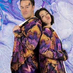May include: Two people wearing purple and gold hooded jackets with a floral pattern. The jackets have a sherpa lining. The background is a blue and purple abstract painting.