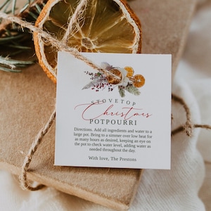 Könnte beinhalten: Eine braune Geschenkbox, die mit Schnur gebunden und mit getrockneten Orangenscheiben und immergrünen Zweigen verziert ist. Ein weißes Etikett, das an der Box befestigt ist, lautet "Stovetop Christmas Potpourri" mit Gebrauchsanweisungen und der Nachricht "Mit Liebe, The Prestons".