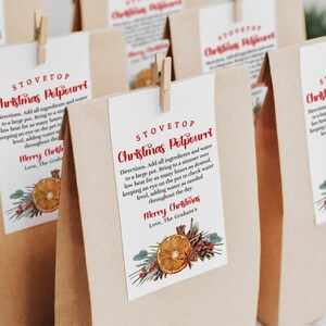Könnte beinhalten: Sechs braune Papiertüten mit roten und weißen Etiketten, auf denen "Stovetop Christmas Pelpeurri" steht. Die Etiketten zeigen eine rote und weiße Illustration einer Orangenscheibe, Kiefernnadeln und Zimtstangen.