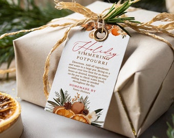 May include: A brown paper gift box tied with twine and a sprig of rosemary. A white tag with a red and black handwritten title "Holiday Simmering Potpourri" and instructions for use is attached to the box. The tag features a watercolour illustration of oranges, cinnamon sticks, and cloves.