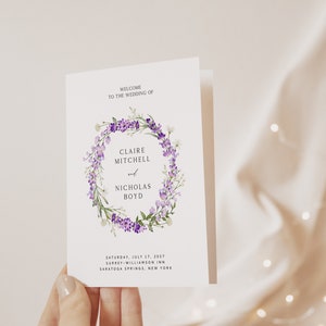 Peut inclure: Un programme de mariage blanc avec un motif de couronne florale violette. Le texte indique "Bienvenue au mariage de Claire Mitchell et Nicholas Boyd" et comprend la date, le lieu et la ville.