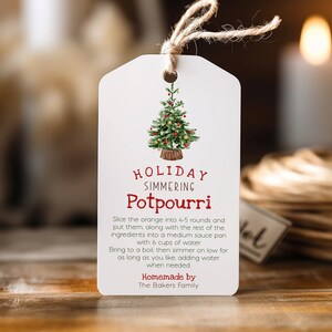 Könnte beinhalten: Ein weißer Geschenkanhänger mit einer Illustration eines grünen Weihnachtsbaums und rotem Text, der "HOLIDAY SIMMERING Potpourri" lautet. Der Text unter dem Titel enthält Anweisungen zur Herstellung eines Potpourris, einschließlich der Verwendung von 6 Tassen Wasser. Der Anhänger enthält auch den Text "Homemade by The Bakers Family".