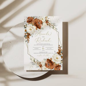 May include: Wedding invitation featuring the names "Amanda and Richard" in elegant script. The invitation is adorned with watercolor floral arrangements in shades of white, brown, and green, set within a geometric gold frame. The date is August 16, 2024.