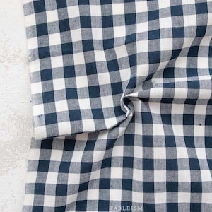 May include: A close-up of a navy blue and white checkered fabric. The fabric is folded and draped, showing the texture and pattern. The pattern is a classic gingham design, with evenly spaced squares.