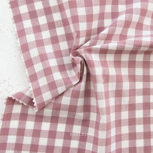 May include: Close-up of a fabric with a pink and white gingham pattern. The fabric is folded, showing the texture and weave. The edge of the fabric is unfinished. The word "FABLEIS" is printed on the fabric.