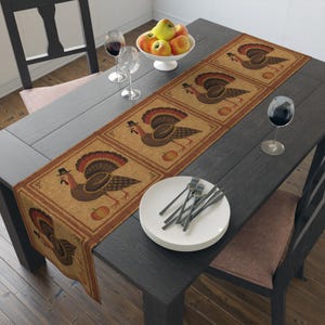 May include: A rectangular table runner featuring a repeating pattern of brown turkeys wearing black hats, each accompanied by an orange pumpkin, set against a tan background with a dark brown border, displayed on a dark wooden dining table.