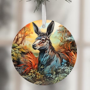 May include: A round Christmas bauble featuring a colourful illustration of a deer with large ears in a woodland setting. The deer is blue, black, and white, and the background is a mix of greens, yellows, and oranges.