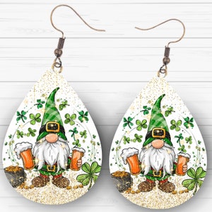 Puede incluir: Un par de pendientes en forma de lágrima con fondo blanco y purpurina dorada. Cada pendiente presenta un gnomo verde sosteniendo una jarra de cerveza, rodeado de tréboles verdes y monedas de oro.