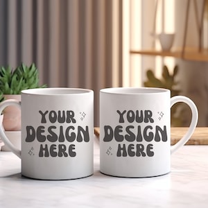 May include: Two white ceramic mugs with black text that reads "Your Design Here" on a white marble surface.