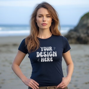 Könnte beinhalten: Ein marineblaues T-Shirt mit dem weißen Text "YOUR DESIGN HERE" und zwei kleinen Stern-Grafiken. Das Shirt hat kurze Ärmel und einen Rundhalsausschnitt. Das Model steht an einem Strand.