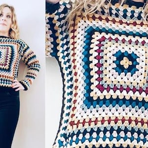 Könnte beinhalten: Ein mehrfarbiger Häkelpullover mit einem quadratischen Muster in der Mitte. Der Pullover hat eine Mischung aus Farben, darunter Blau, Creme, Braun und Burgunderrot. Die Ärmel und der Halsausschnitt sind schwarz.