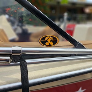 May include: A close-up of a boat with a black and yellow sticker that says "Power Slot" with a propeller symbol. The boat has a brown leather seat and a silver metal railing.