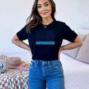 May include: A black t-shirt with a graphic print of the word "amused" repeated four times in a gradient of blue and black.