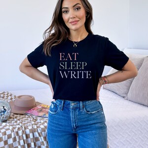 May include: A black t-shirt with the text "EAT SLEEP WRITE" in pink, green, and gray lettering.