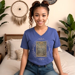 May include: A royal blue V-neck t-shirt featuring a vintage tarot card design with a skeleton with outstretched arms and the text "The Judgment".