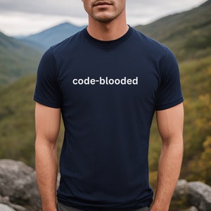 Könnte beinhalten: Marineblaues T-Shirt mit Rundhalsausschnitt und dem weißen Text "code-blooded". Das T-Shirt besteht aus einem weichen Material und wird im Freien mit einem Bergpanorama getragen.