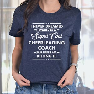 May include: A navy blue t-shirt with white text that reads "I never dreamed I would be a Super Cool Cheerleading Coach but here I am killing it!"