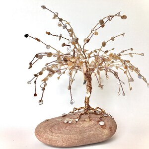 Peut inclure: Une sculpture d'arbre en fil de fer avec une base brune et des décorations en coquillages blancs et bruns. L'arbre est fait de fil de fer et a un aspect naturel et organique.