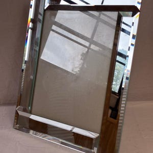 May include: A rectangular picture frame featuring a reflective mirrored glass border with beveled edges. The frame has a clear glass center panel and a neutral-colored backing board, designed to hold a photograph or artwork in a vertical orientation.