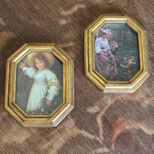 May include: Two octagonal picture frames with a metallic gold finish. The left frame contains a portrait of a child in a white dress and straw hat. The right frame displays a scene of an adult and two children in a garden setting.