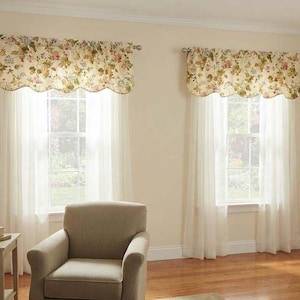 May include: Two windows featuring cream-colored valances with a multi-colored floral pattern and scalloped edges, paired with sheer white curtains hanging from silver rods. The floral print includes shades of pink, green, and blue on a light background.