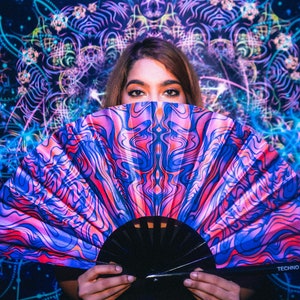 May include: A woman holds a colorful hand fan with a swirling pattern in shades of pink, blue, and purple. The fan has a black handle with the text "Techno Hype" printed on it. The background is a dark blue with a glowing mandala pattern.