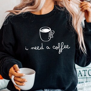 May include: A black sweatshirt with a white graphic of a coffee cup and the text "i need a coffee".