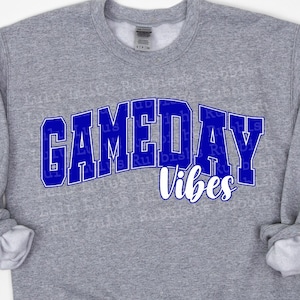 Op de afbeelding: Grijs sweatshirt met de tekst "GAMEDAY vibes" in blauwe letters.