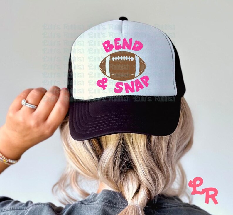 May include: A black and white trucker hat with a white mesh back. The front of the hat has a pink and white design that says "Bend & Snap" with a brown football graphic.