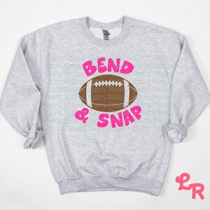 May include: Gray sweatshirt with a pink graphic of a football and the text "Bend & Snap".