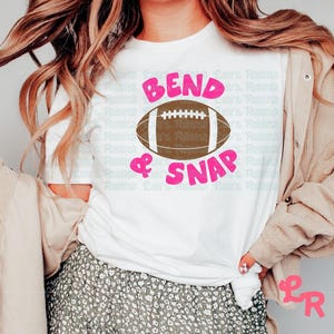 May include: White t-shirt with the text "Bend & Snap" in pink letters and a brown football graphic.