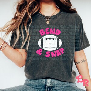 May include: A dark gray t-shirt with the text "Bend & Snap" in pink letters and a white football graphic.