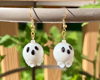 Op de afbeelding: Een paar gouden oorhangers met witte spookbedels. Elk spook heeft twee zwarte ogen en een kleine mond.