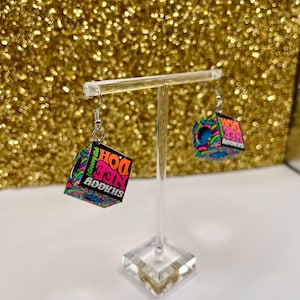 Könnte beinhalten: Ein Paar Hängeohrringe mit einem schwarzen Würfel mit bunten psychedelischen Grafiken und dem Text "Shaggy, Nice, Doh!" auf dem einen Ohrring und "Groovy, Doh!" auf dem anderen.