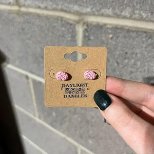 May include: Pink brain-shaped stud earrings on a brown card with the text "Daylight Dangles". The earrings are displayed against a grey brick wall.